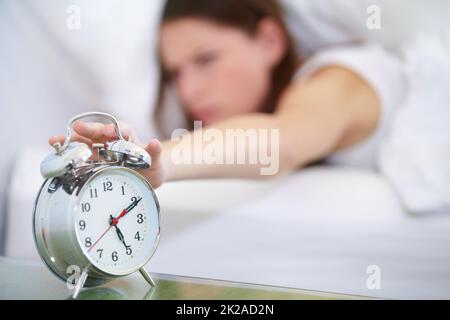 Not yet. A young woman pressing the stop button on her alarm clock. Stock Photo