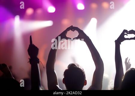 Showing some love for the band. Rearview of people in the audience at a music concert holding up their hands in a heart symbol. Stock Photo