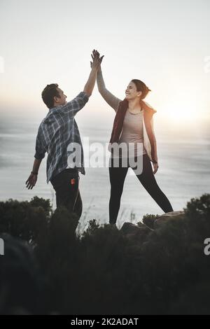 This couple conquered the mountain. Shot of a young couple high fiving after making it to the top of the mountain. Stock Photo