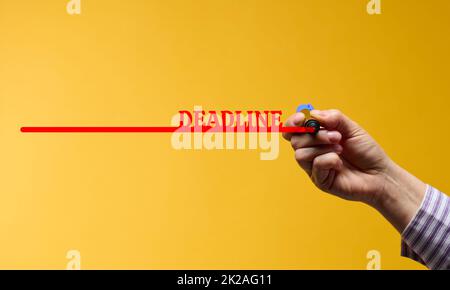 red line with the inscription deadline and a female hand with a marker on a yellow background. The concept of setting time limits Stock Photo
