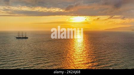 Romantic golden sunset on the sea with a yacht against the background of mountains and orange clouds, a calm scene of a warm peaceful evening Stock Photo