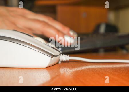 Close-up of a computer mouse and a blurry background in the background - a female hand working on the keyboard. Work from home during covid-19, Selective focus, background blur Stock Photo