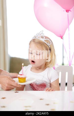 Her first birthday. Shot of a cute young girl blowing out a candle on a cupcake. Stock Photo