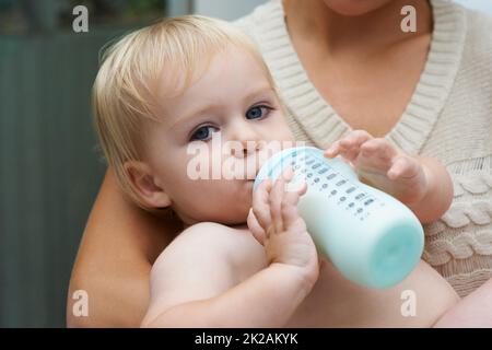 Safe in his mothers arms. A baby boy drinking milk from his bottle while being held by his mother. Stock Photo