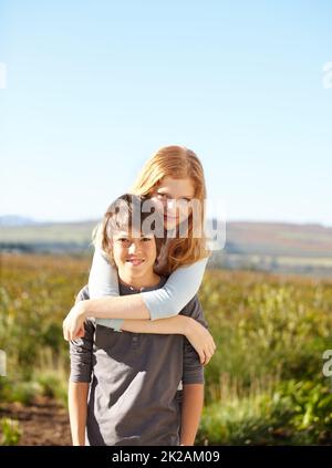 Sisterly love. Portrait of a young boy giving his sister a piggyback in the garden. Stock Photo
