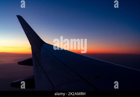 Wing of plane with sunrise skyline. Airplane flying in the sky. Scenic view from airplane window. Commercial airline flight. Plane wing above clouds. International flight. Travel abroad after covid-19 Stock Photo