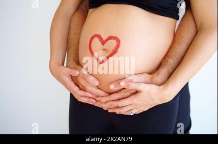 You have my support -fatherhood. Pregnant womanamp039s belly with her partneramp039s hands wrapped around her and a heart shape painted on it. Stock Photo
