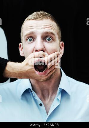 I will not be silenced. A distraught looking man with his mouth showing through the hand trying to silence him. Stock Photo