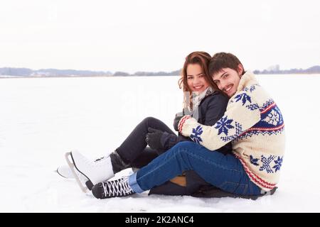 We love this time of year. Sweet young couple in ice skates cuddling on the ice of a frozen natural lake outdoors.