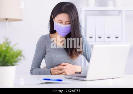 Young woman suffering from abdominal pain in office Stock Photo