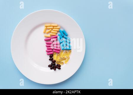 White plate with pills of nutritional supplements in different bright colors. Blue background, place for an inscription. Stock Photo