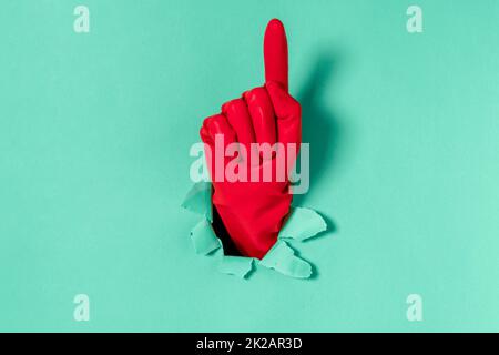 Hand sticking out of a torn hole in a blue paper background, attention gesture Stock Photo