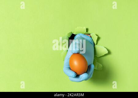 A man holds a chicken egg in his hand after breaking through a green paper wall Stock Photo