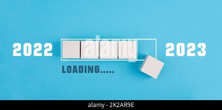 The new year 2023 is standing on a blue colored background, loading bar with wooden cubes, calendar date Stock Photo