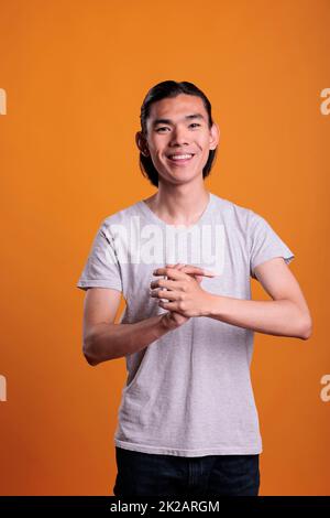 Young adult cheerful smiling asian man clapping hands portrait. Positive teenager with joyful facial expression laughing, applauding handsome person standing, medium shot Stock Photo
