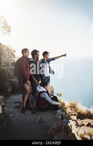 I can see my house from here. Shot of a young man pointing something out to his friends while on a mountain hike. Stock Photo