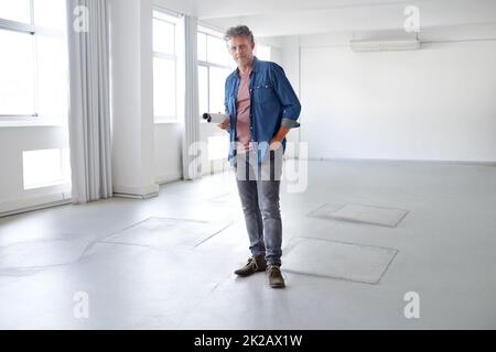 Envisioning great things for this space. A portrait of a mature man standing in an empty room holding building plans. Stock Photo