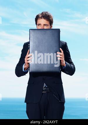 Young business man covering his face with briefcase. Young business man covering his face with briefcase against the sea. Stock Photo