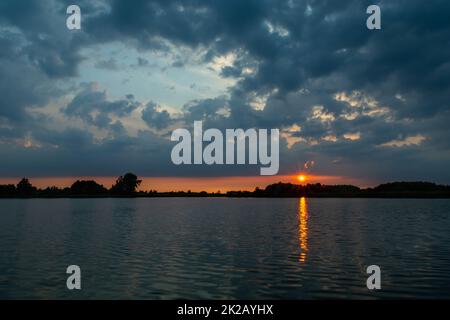 Dark clouds and sunset over the lake Stock Photo