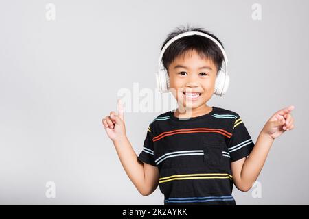 Little cute kid boy 5-6 years old listen music in wireless headphones in studio shot isolated.Little cute kid boy 5-6 years old listen music in wireless headphones in studio shot isolated on white background, happy Asian children smiling listening audio a Stock Photo