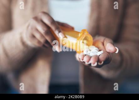 I cant handle the stress today. Cropped shot of an unrecognizable woman sitting alone and taking pills out of a pill bottle in her living room. Stock Photo