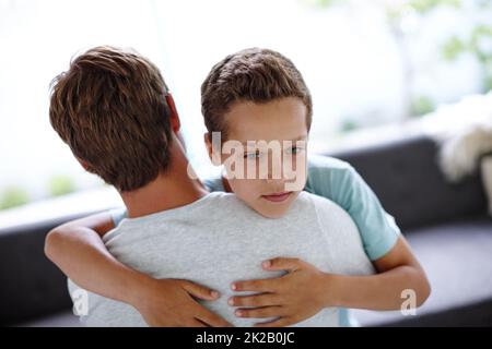 Hes missing Mom. Shot of a sad little boy hugging his father at home. Stock Photo