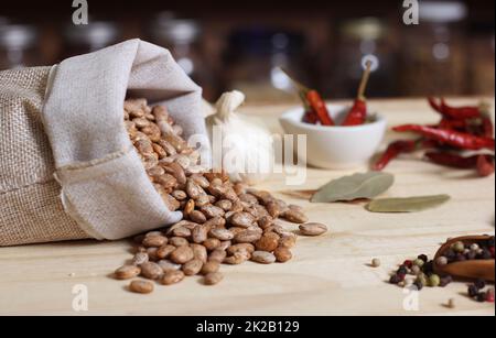 Burlap Sack of Pinto Beans on Table with Spices in Background Stock Photo