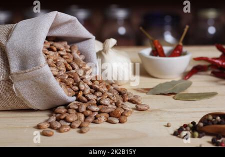 Burlap Sack of Pinto Beans on Table with Spices in Background Stock Photo