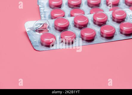 Take pill concept. Pink tablets pills in blister pack on pink background. Prescription drug. Pharmaceutical industry. Pill reminder or medication reminder background. Vitamin, mineral, and supplement. Stock Photo