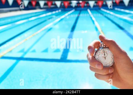 Time trials. Cropped shot a hand holding a stopwatch infront of a swimming pool. Stock Photo