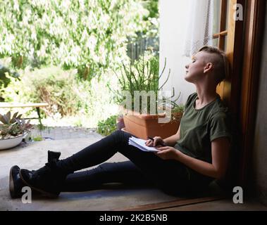 Drifting amongst the ideas. an attractive young woman sitting outside on the porch writing in a notepad. Stock Photo