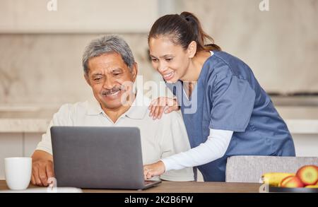 Happy nurse help senior man with laptop, showing how to make a video call or search the internet in an assisted living home. Senior patient enjoying Stock Photo