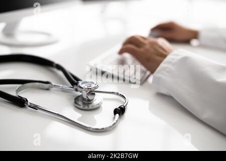 View Of Stethoscope With Doctor Using Computer Keyboard Stock Photo