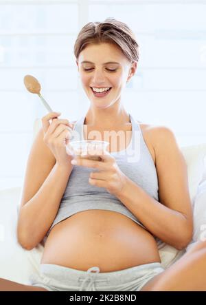 Mommy needs some sugar. A happy young pregnant woman eating a small bowl of pudding. Stock Photo