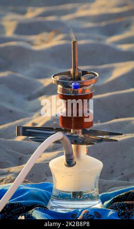 A hookah or shisha stands on a towel on the beach. Stock Photo