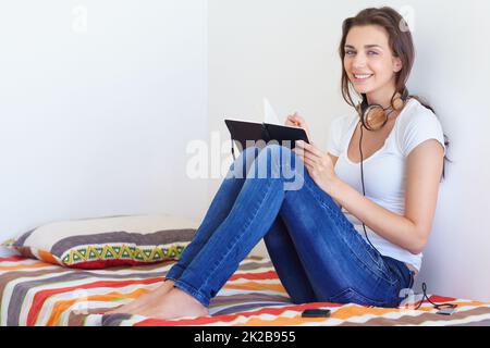 Letting the creativity flow. A teenage girl sitting on her bed writing in her notepad with ehr headphones around her neck. Stock Photo