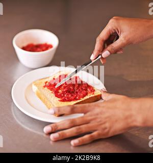 Fruity treat for breakfast. Cropped shot of a woman spreading fruity jam onto toast. Stock Photo