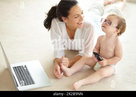 Shes destined for great things. A cute little baby wearing her mothers glasses and holding a cellphone while sitting in front of a laptop. Stock Photo