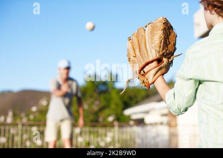 Getting to grips with his mitt. Cropped shot of a father and son throwing the baseball outdoors in the yard. Stock Photo