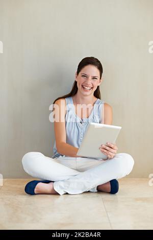 This is so easy to use. A beautiful young woman using her tablet while sitting on the floor. Stock Photo