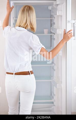 Time to do some serious shopping. Rearview of a young woman looking in her empty fridge. Stock Photo