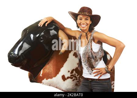 Not afraid to take on the bull. Studio shot of a beautiful young cowgirl standing next to a mechanical bull against a white background. Stock Photo