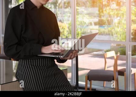 Barista cafe owner working on laptop computer while standing in coffee shop, counting profit Stock Photo