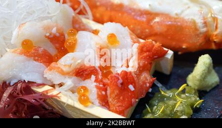 Sashimi Alaska King Crab top with  Ikura on wooden plate. Served with maufunori seaweed, shredded radish, kizami wasabi and fresh wasabi. Stock Photo