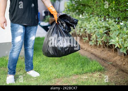 Woman holding black plastic trash bin bags of garbage on the pavement, clean environment concept. Stock Photo