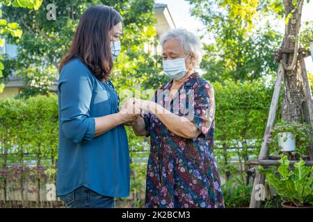 Caregiver help Asian elderly woman while walking with happy in nature park. Stock Photo