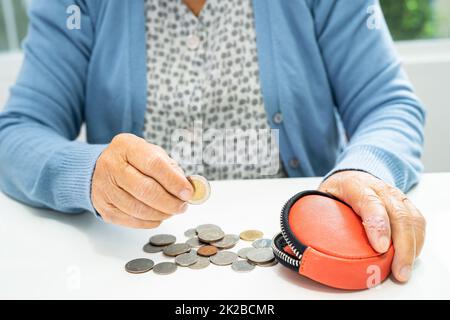 Asian senior or elderly old lady woman holding counting coin money in purse. Poverty, saving problem  in retirement. Stock Photo