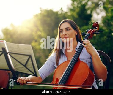 Music is something you hear and feel. Cropped shot of a beautiful woman playing a cello in the backyard. Stock Photo