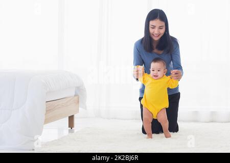 baby girl taking first steps learning to walk with mom Stock Photo