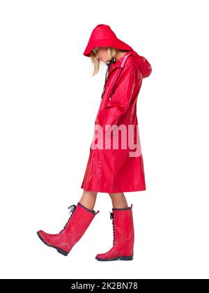 Why does it always rain on me. Woman wearing a red raincoat, hat and boots with her head looking down and hands in her pockets- full length. Stock Photo
